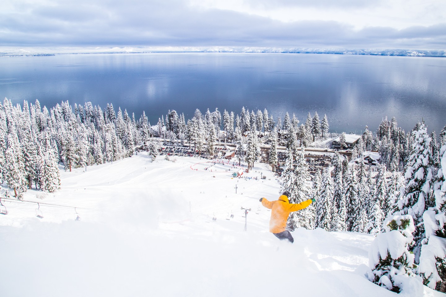 A person snowboarding on a resort facing a lake