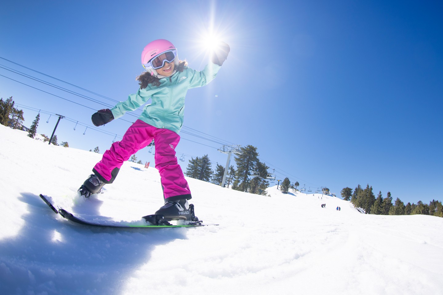 child on skis smiling down at camera while in pizza, clear blue skies behind her